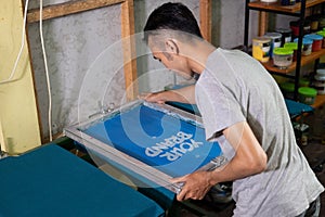 Asian male worker sets up and installs the silkscreen frame on the hinges