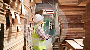 Asian male worker in uniform inspects with laptop at paper factory warehouse.