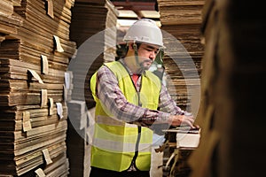 Asian male worker in uniform inspects with laptop at paper factory warehouse