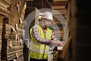 Asian male worker in uniform inspects with laptop at paper factory warehouse