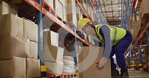 Asian male worker wearing safety suit with helmet and carrying boxes in warehouse