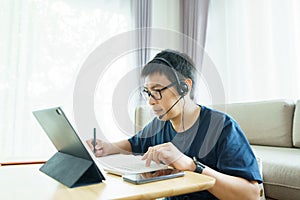 Asian man aged 30-40 years using tablet, watching lesson online course communicate by conference video call from home, e-learning photo