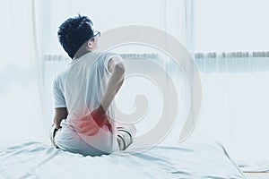 Asian man back pain and sit on bed in bedroom