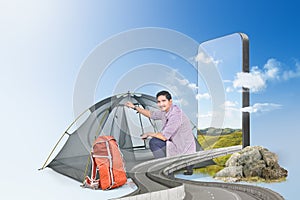 Asian man with a backpack setting up a tent with a hill view on the mobile phone screen