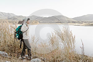 Asian man backpacking in Long-sleeved shirt and grey hat standing on the floor looking Landscape view and mountains at Maetip