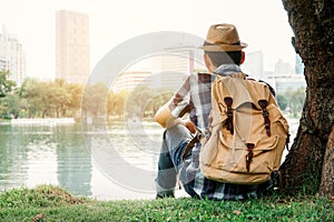 Asian man backpacking sitting under the tree on park background