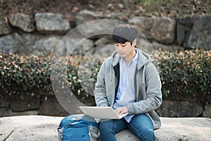 Asian man backpacking using laptop.