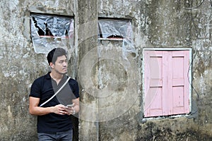 Asian man in black shirt and mobile phone in hand standing on old wall.