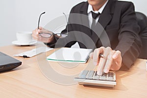 Asian man in black suit holding pen writing a tax report lead to liquidation and using calculator