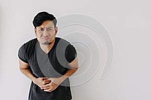 Asian man in black t-shirt feeling sick and stomach ache isolated on white.