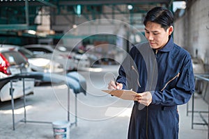 Asian man car mechanic is checking report in auto repair shop