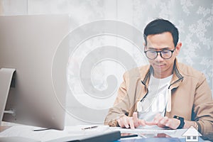 Asian man in casual clothing using a laptop communicates on the internet with the customer at  kitchen table at home. concept work