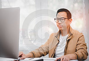 Asian man in casual clothing using a laptop communicates on the internet with the customer at  kitchen table at home. concept work