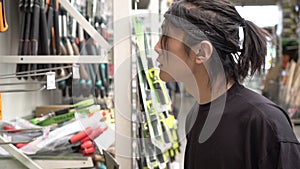 Asian man chooses construction tools in a hardware store. A man chooses an ax in a supermarket