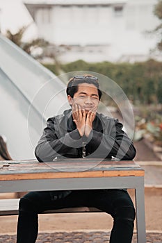 an Asian man with a chubby face wearing sunglasses and a black leather jacket while sitting at a cafe table