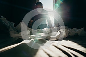 Asian man cleaning bed in morning. House keeping action. Bedroom gainst the sun light photo