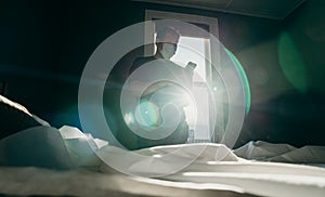 Asian man cleaning bed in morning and using cellphone. House keeping action. Bedroom gainst the sun light photo