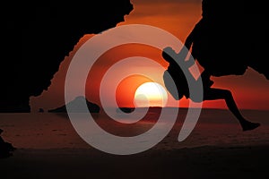 Asian man climbing a cliff by the sea As the sun sets around the islands in the Gulf of Thailand