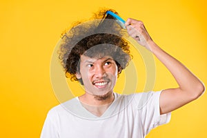 Asian man combing curly hair on yellow background