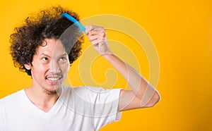 Asian man combing curly hair on yellow background