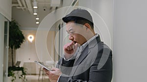 Asian man in corporate office using mobile phone upset thoughtful chinese korean middle-aged businessman texting