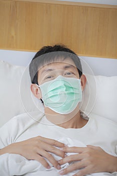 Asian man coughing and suffering in medical mask inside bedroom