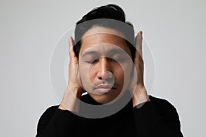 Asian man is covering ears and closing his eyes. Mental health issues.