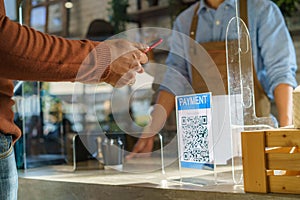 Asian man customer using mobile scan QR or NFC payment on smart phone paying for her coffee drink in coffee shop and plexi screen