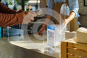 Asian man customer using mobile scan QR or NFC payment on smart phone paying for her coffee drink in coffee shop and plexi screen