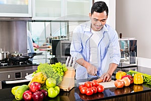 Asian man cutting salad in kitchen