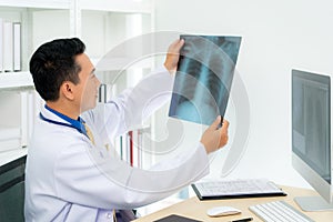 Asian man doctor holding and looking to examining x-ray of the patientâ€™s lungs and brain in a medical clinic at hospital