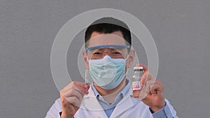 Asian man doctor virologist in medical face mask gloves show bottle of vaccine syringe injection dose