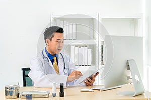 Asian man doctor wears white coat and headset speaking videoconferencing on laptop computer using online video call consultation