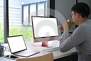 Asian man drinking coffee and working with modern devices.