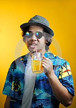 Asian Man Drinking Orange Juice Wearing Fedora Hat and Sunglasses against Yellow Background