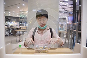 Asian man eating a meal in food court and washing hand with alcohol gel to sanitize Coronavirus COVID-19. New normal redesigned