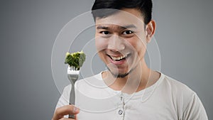 An Asian man eats broccoli.