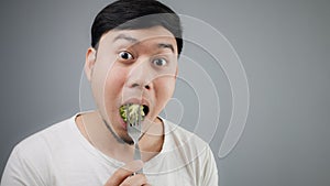 An Asian man eats broccoli.