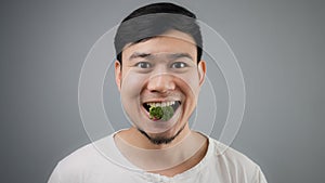 An Asian man eats broccoli.