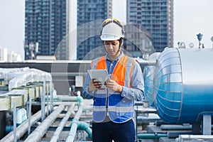 Asian man engineer holding tablet working at rooftop building construction. Male technician worker working checking hvac of office