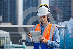 Asian man engineer holding tablet working at rooftop building construction. Male technician worker working checking hvac of office