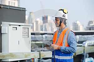 Asian man engineer holding tablet working at rooftop building construction. Male technician worker working checking hvac of office