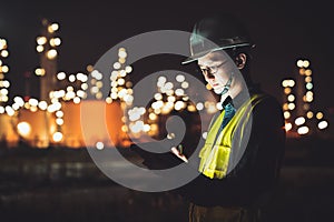 Asian man engineer using digital tablet working late night shift at petroleum oil refinery in industrial estate. Chemical engineer