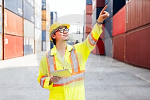 Asian man engineer working with tablet and point up at containers at a container yard. Shipping business management.