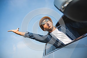 An Asian man is enjoying his trip. He stretches out of the car window to make him look happy