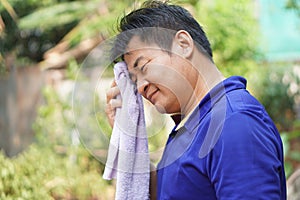 Asian man feel headache and unwell from hot weather condition, use cool wet cloth to wipe face for relief symptom