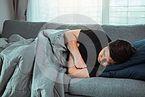 Asian man feel the illness while he was cold lying on the sofa and wearing a blanket at his house