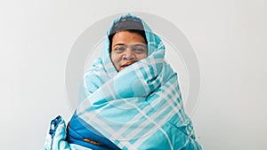 Asian man feeling cold and covered under a blanket on the bed in the morning