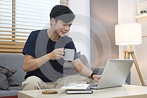 Asian man freelancer in casual clothes browsing internet, replies to email or working online via laptop computer photo