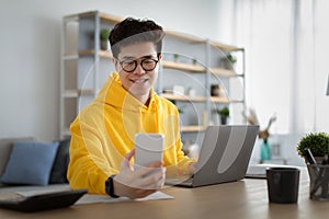 Asian man in glasses sitting at desk using cell phone